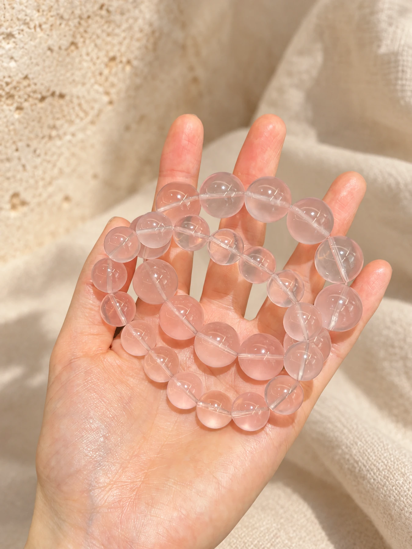 Several pale pink crystal bead bracelets held in a hand