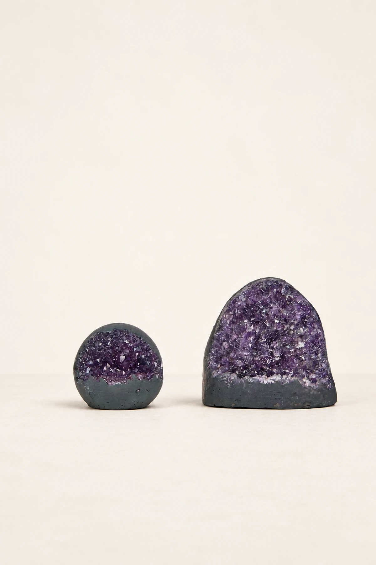 Two purple crystal geodes on a pale reflective surface