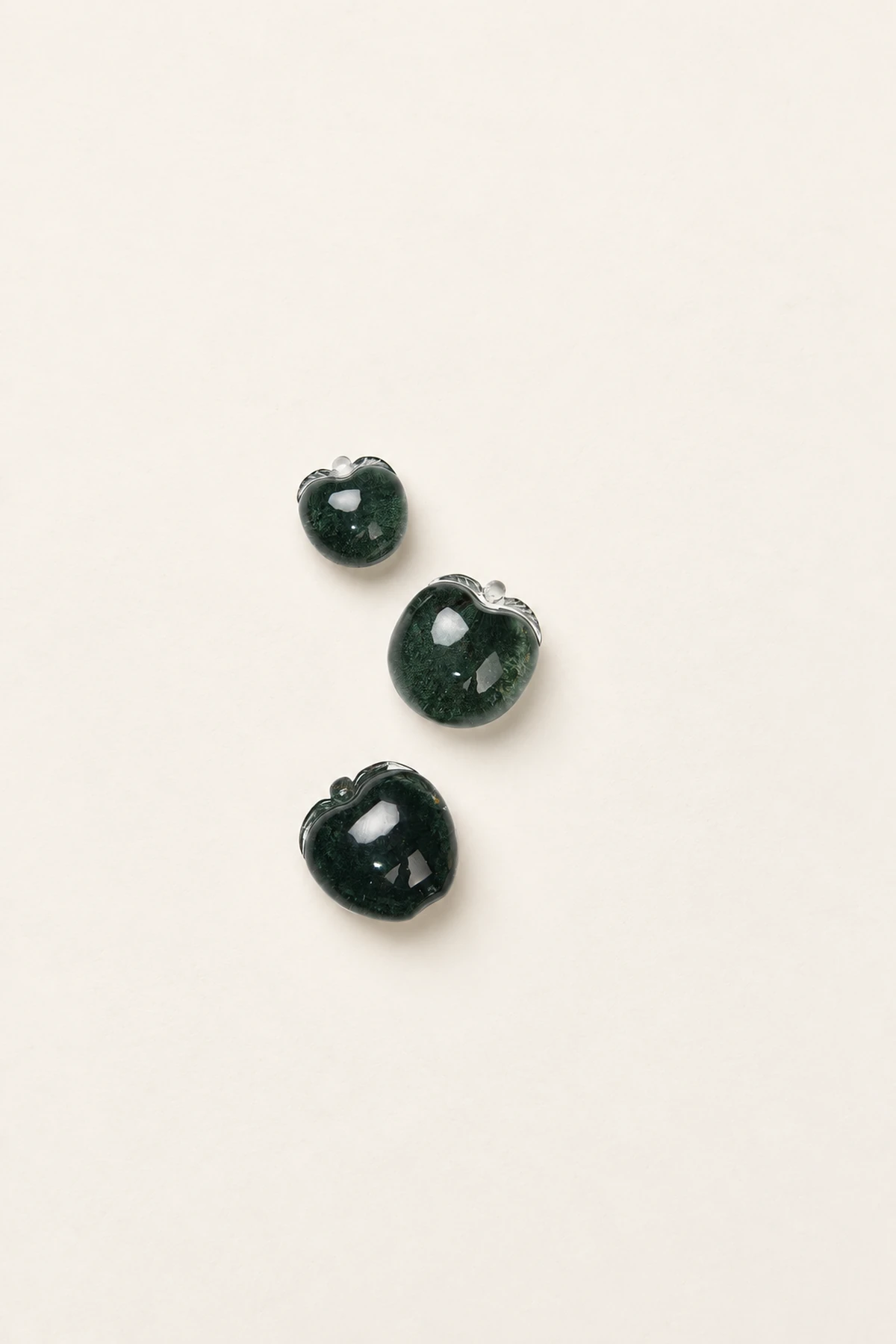 Three dark green carved pendants on a pale surface