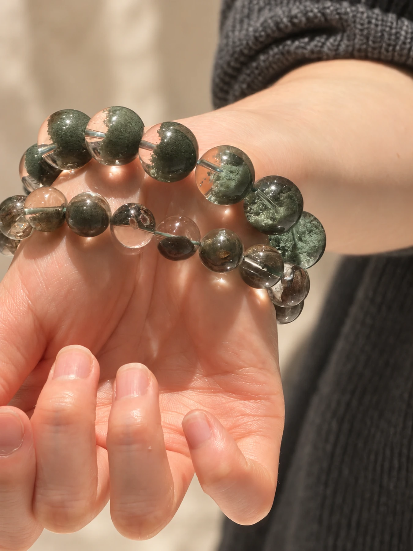 Green-inclusion quartz bead bracelets held in a hand